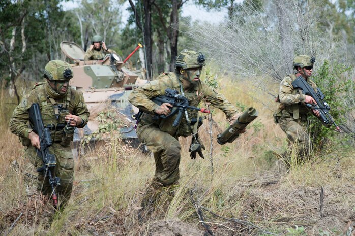Australian soldiers run through grassland during training.