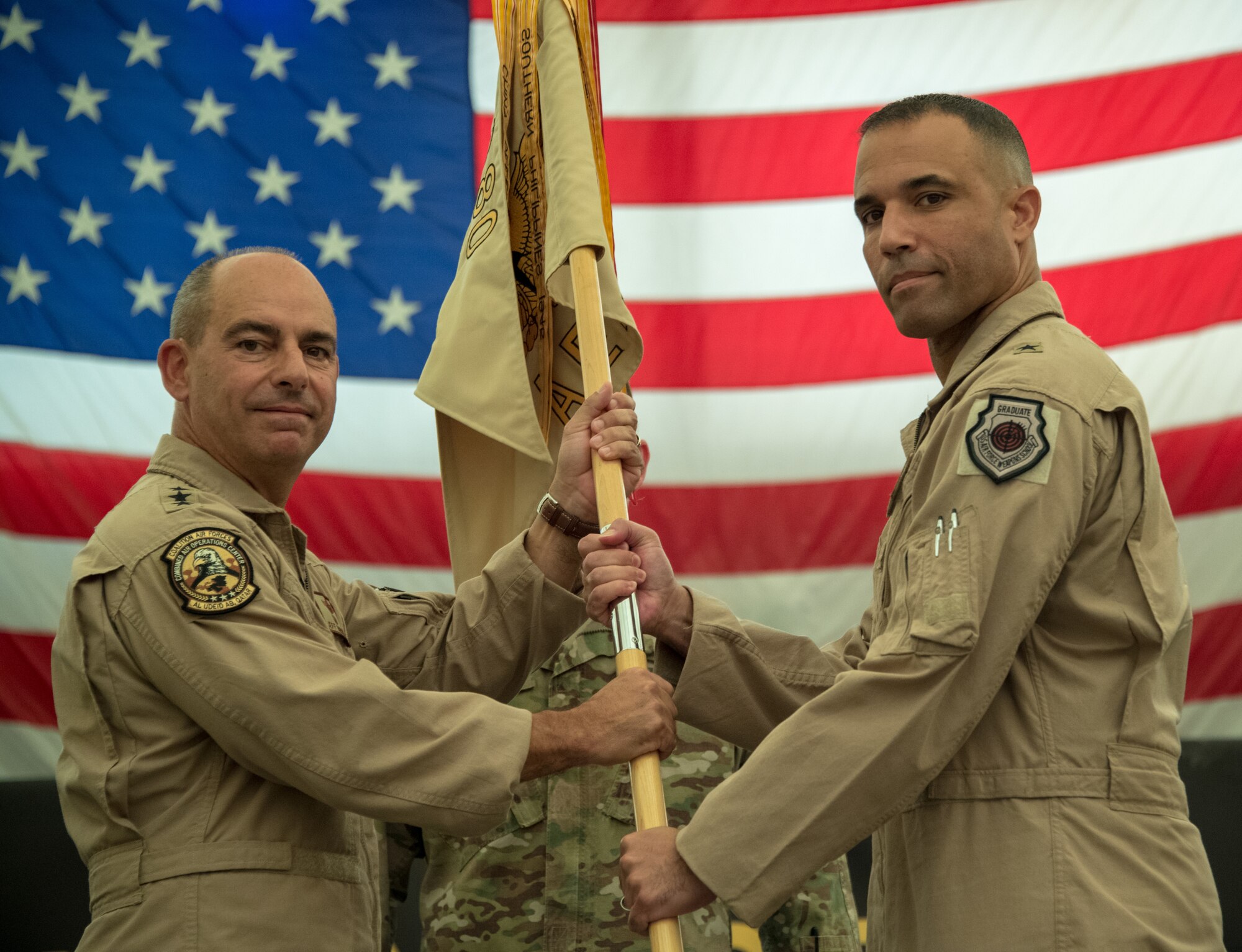 U.S. Air Force Lt. General Jeffrey L. Harrigian, commander of the U.S. Air Force Central Command, hands the 380th Air Expeditionary Wing’s guidon to incoming Commander Brig. Gen. Adrian L. Spain during a change of command ceremony at Al Dhafra Air Base, July 2, 2018. (U.S. Air Force photo by Tech. Sgt. Nieko Carzis)