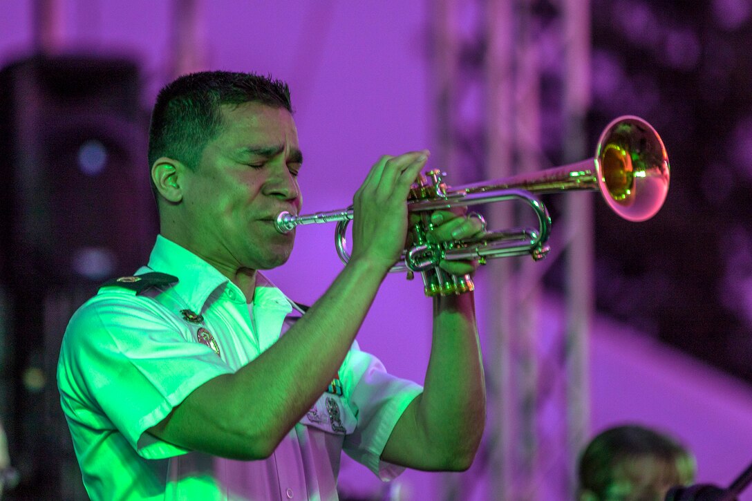 A soldier, bathed in green light, plays the trumpet against a light purple illuminated background.