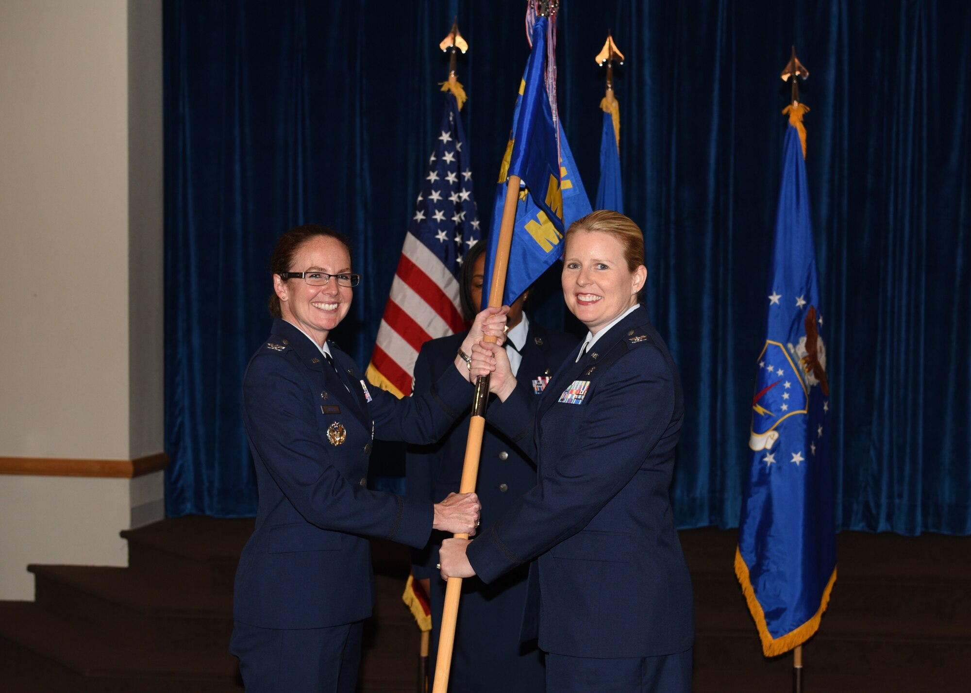 Colonel Stacy Jo Huser, 90th Missile Wing commander, passes the guidon to Col. Kristine Hackett, 90th Medical Group commander, during the 90th MDG change of command ceremony June 29, 2018, at F.E. Warren Air Force Base, Wyo. The ceremony signified the transition of command from Col. Cherron Galluzzo. (U.S. Air Force photo by Airman 1st Class Braydon Williams)