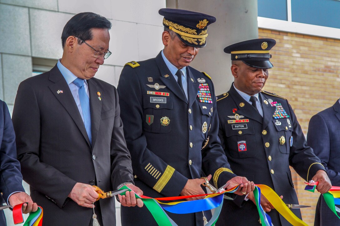 Three people stand shoulder to shoulder and cut a ribbon.