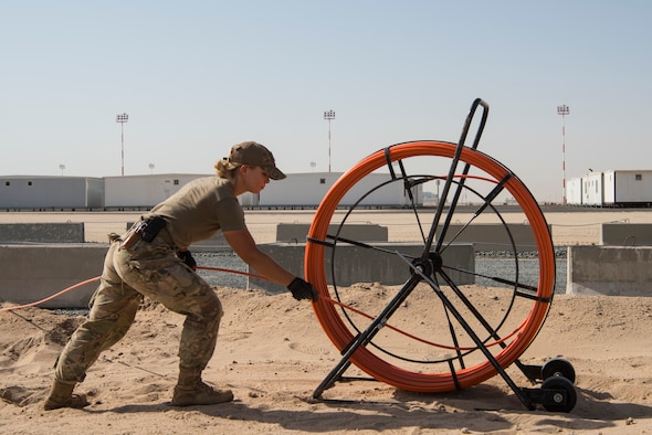 Senior Airman Kelsie Burt, 379th Expeditionary Civil Engineer Squadron cable and antenna systems technician, deployed from Zanesville, Ohio, re-spools communications line at Cargo City, located at Abdullah Al Mubarak Air Base, Kuwait, June 25, 2018. Burt and her team are forward deployed from Al Udeid Air Base, Qatar. (U.S. Air Force photo by Staff Sgt. Joshua King)