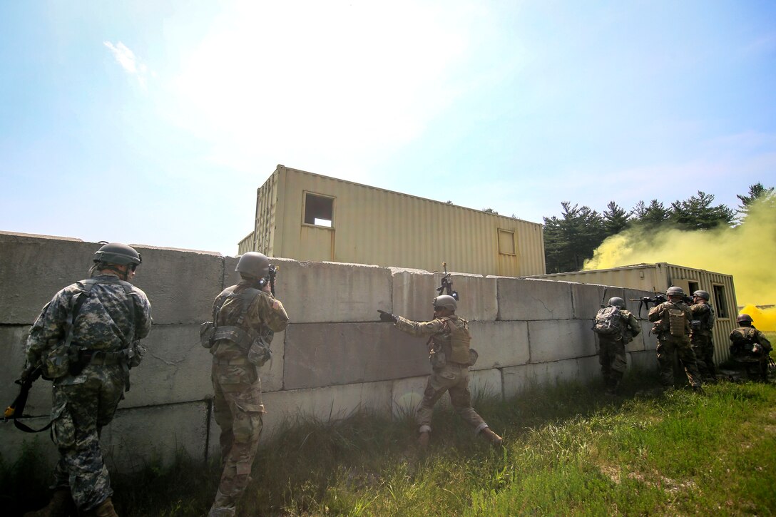 Soldiers move cautiously along a wall under the cover of smoke.