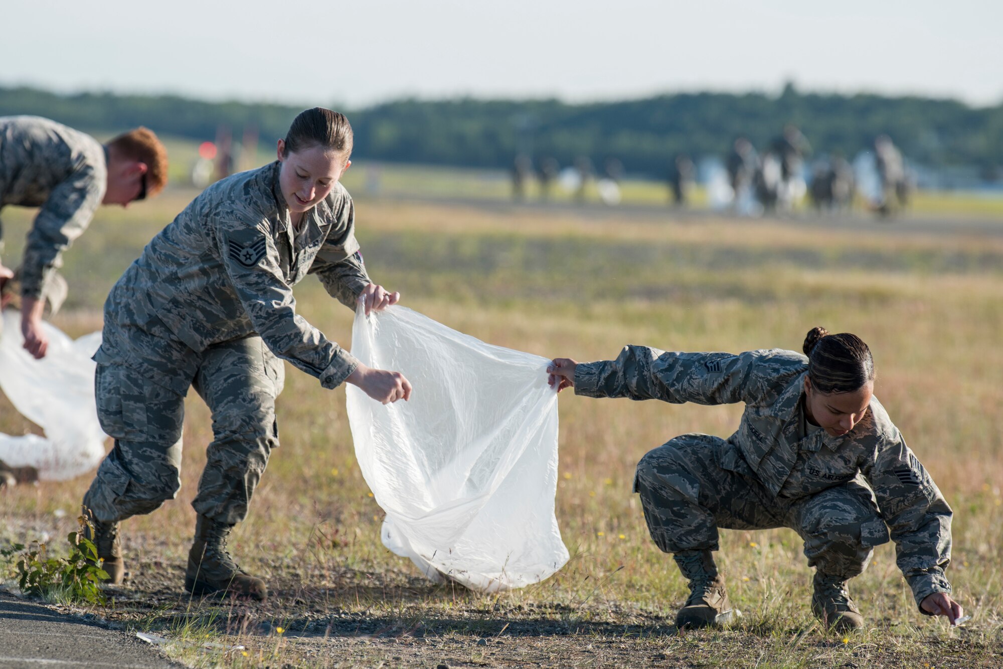 Staff Sgts. Kelsey Padula and Amanda Woodell, both 3rd Munitions Squadron muntions systems crew chiefs, pick up trash during a foreign object and debris walk at Joint Base Elmendorf-Richardson, Alaska, July 2, 2018. The JBER Airmen conducted the FOD walk after the Arctic Thunder Open House to remove debris that could damage aircraft and hinder mission readiness.