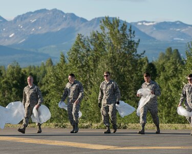 Joint Base Elmendorf-Richardson Airmen walk onto the flight line as they prepare to conduct a foreign object and debris walk at JBER, Alaska, July 2, 2018. The Airmen conducted the FOD walk after the Arctic Thunder Open House to remove debris that could damage aircraft and hinder mission readiness.