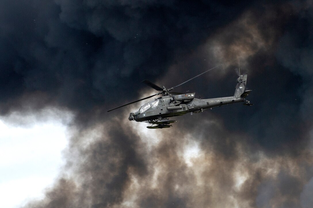 An Army AH-64 attack helicopter flies through smoke.