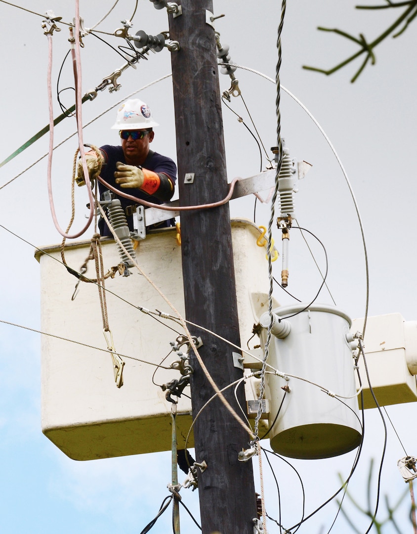 An electrical worker labors on a utility pole, perched high on a bluff, to restore power to 51 clients in Orocovis, Puerto Rico. The workers were contracted by the U.S. Army Corps of Engineers through a mission assignment from the Federal Emergency Management Agency as a result of Hurricane Maria.