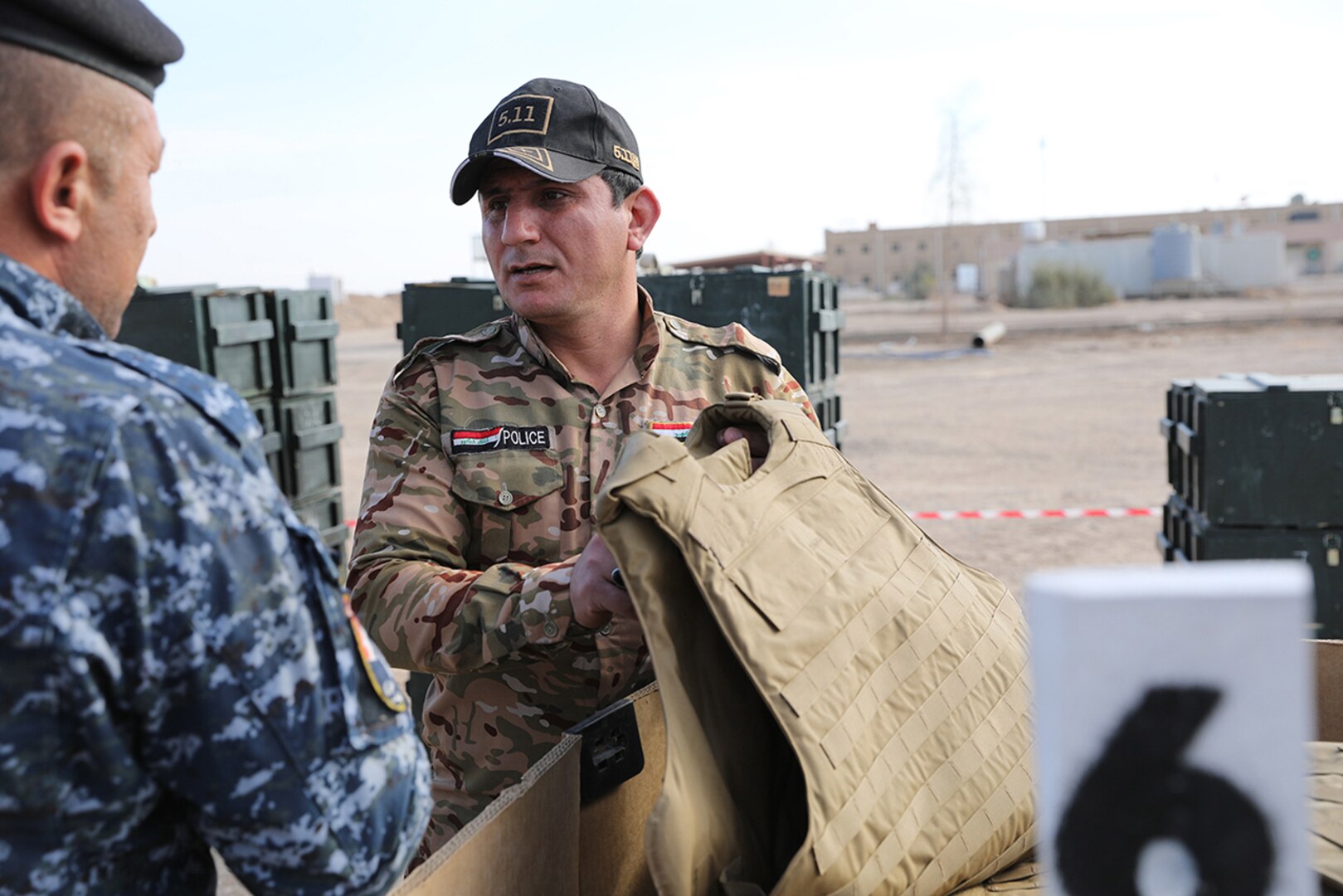 Members of the Iraqi Police look at one ballistic vest from a container during the divestment of organizational clothing and individual equipment to the Iraqi army and police at the Besmaya Range Complex, Iraq. The Coalition is enabling partnered forces to defeat ISIS by providing air, artillery and logistical support on the battlefield.