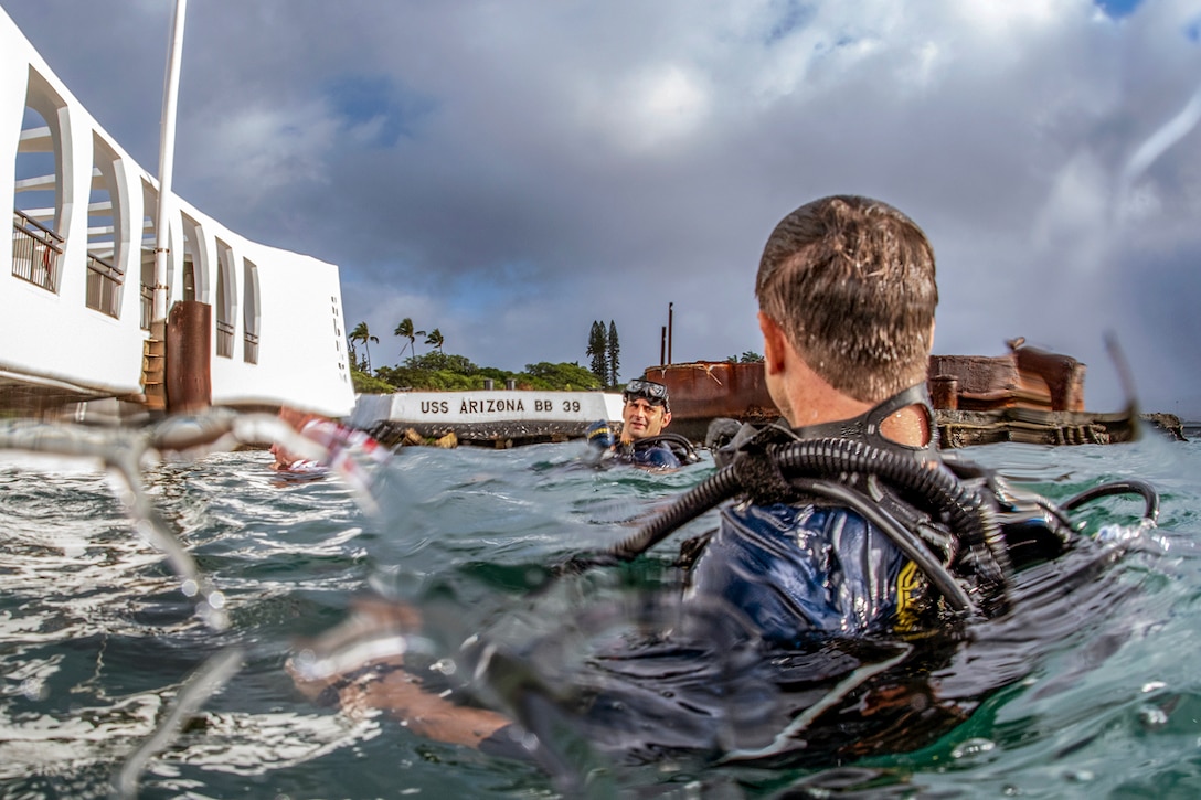 Two divers float on the surface of the water near a structure.