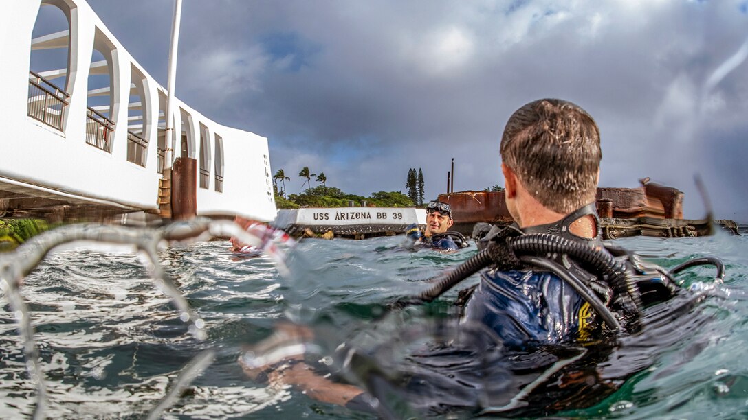 Two divers float on the surface of the water near a structure.