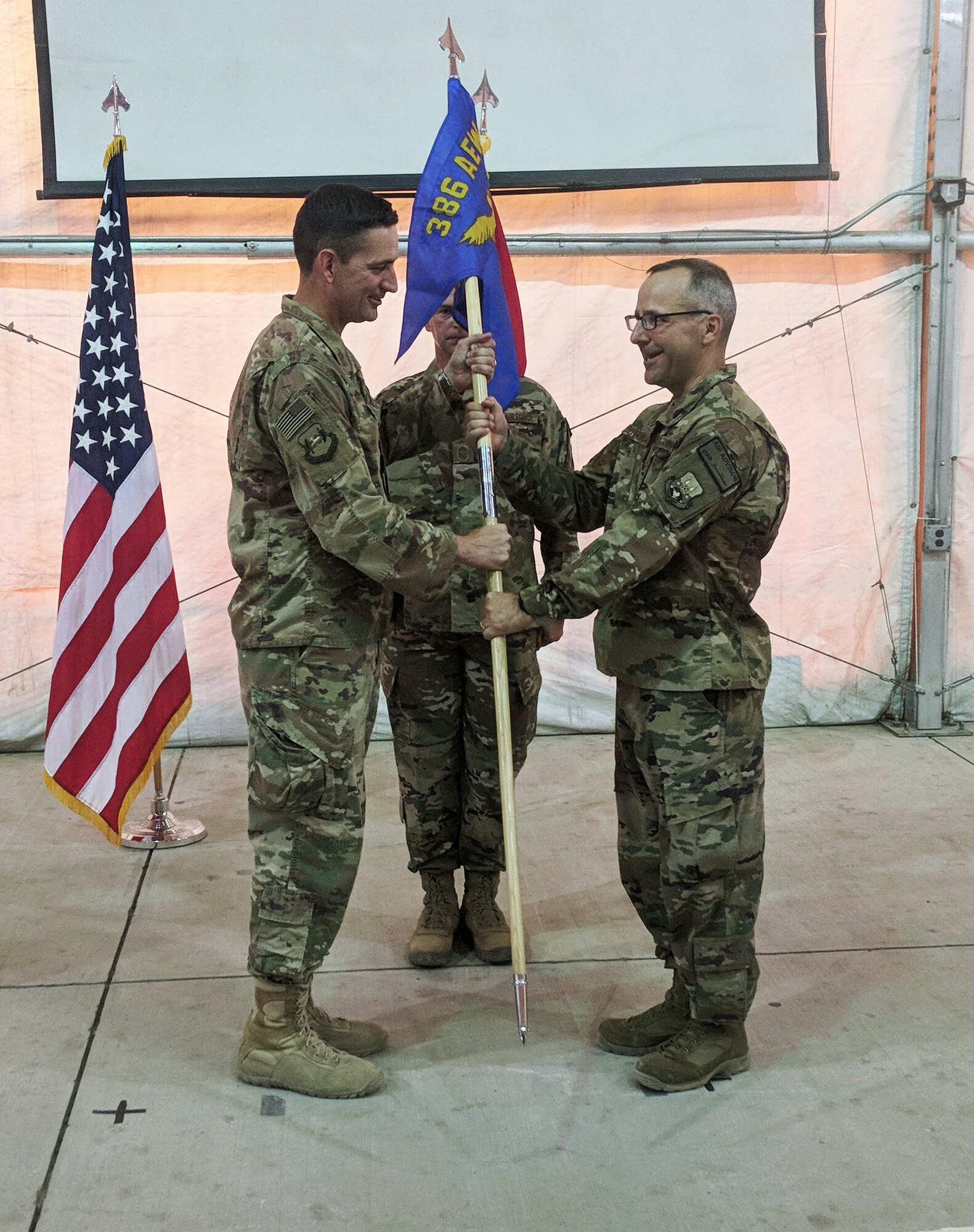 Col. Stephen Hodge, commander of the 386th Air Expeditionary Wing, passes the 370th Air Expeditionary Advisory Group guide-on to Col. Eduardo Defendini during a ceremony in Baghdad, Iraq, July 5. Defendini is a senior navigator with over 2,100 flight hours and experience with over five different aircraft. (Courtesy photo)