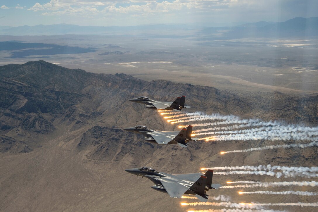 Three aircraft fire flares over a desert.