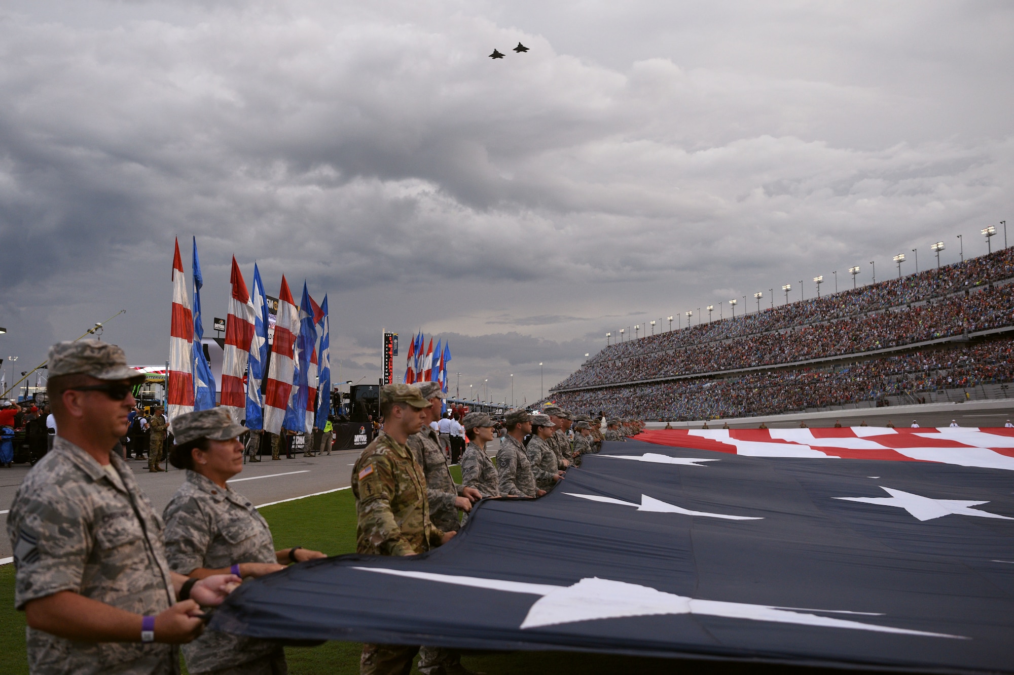 Service members display a 1,000 pound, football field-size American flag during the National Anthem as two F-22 Raptor aircraft conduct a fly over July 7, at the Daytona International Speedway in Daytona Beach, Fla. The F-22's were part of the 43rd Fighter Squadron at Tyndall Air Force Base, Fla. (U.S. Air Force photo by Airman 1st Class Zoe Thacker)
