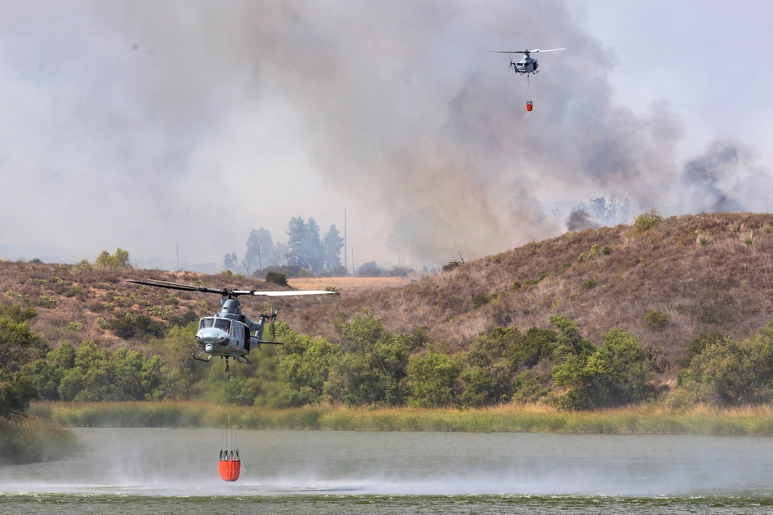 A helicopter flies off after refilling its bucket firefighting system while another helicopter refills.