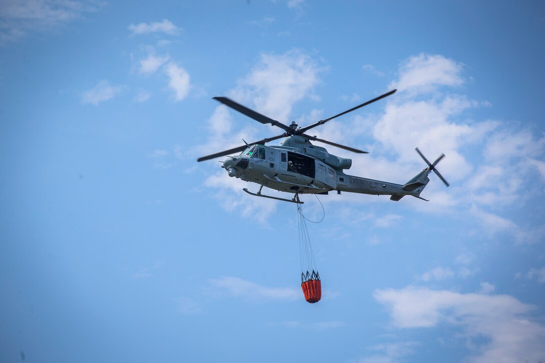 A Marine Corps UH-1 Huey helicopter flies off after refilling a bucket firefighting system.