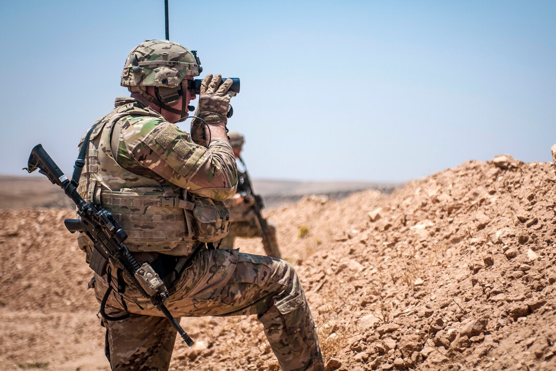 A soldier uses binoculars to scan for movement along the demarcation line.