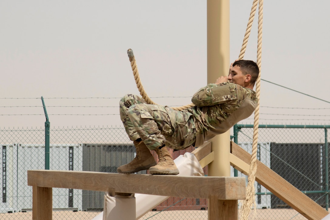 A soldier maneuvers to a beam and sticks the landing on the swing stop jump obstacle.