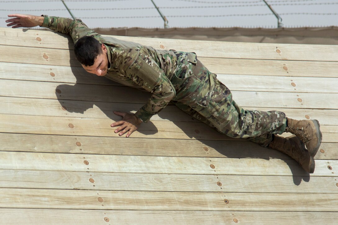 A soldier maneuvers over an incline wall obstacle.