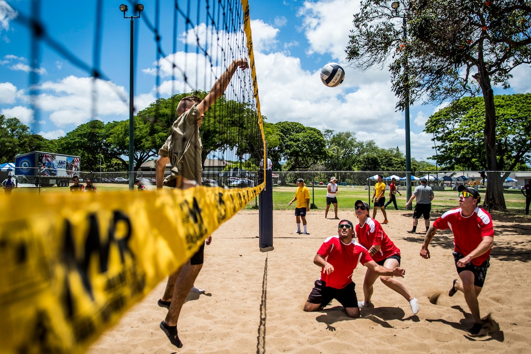 Service members play volleyball on a beach.