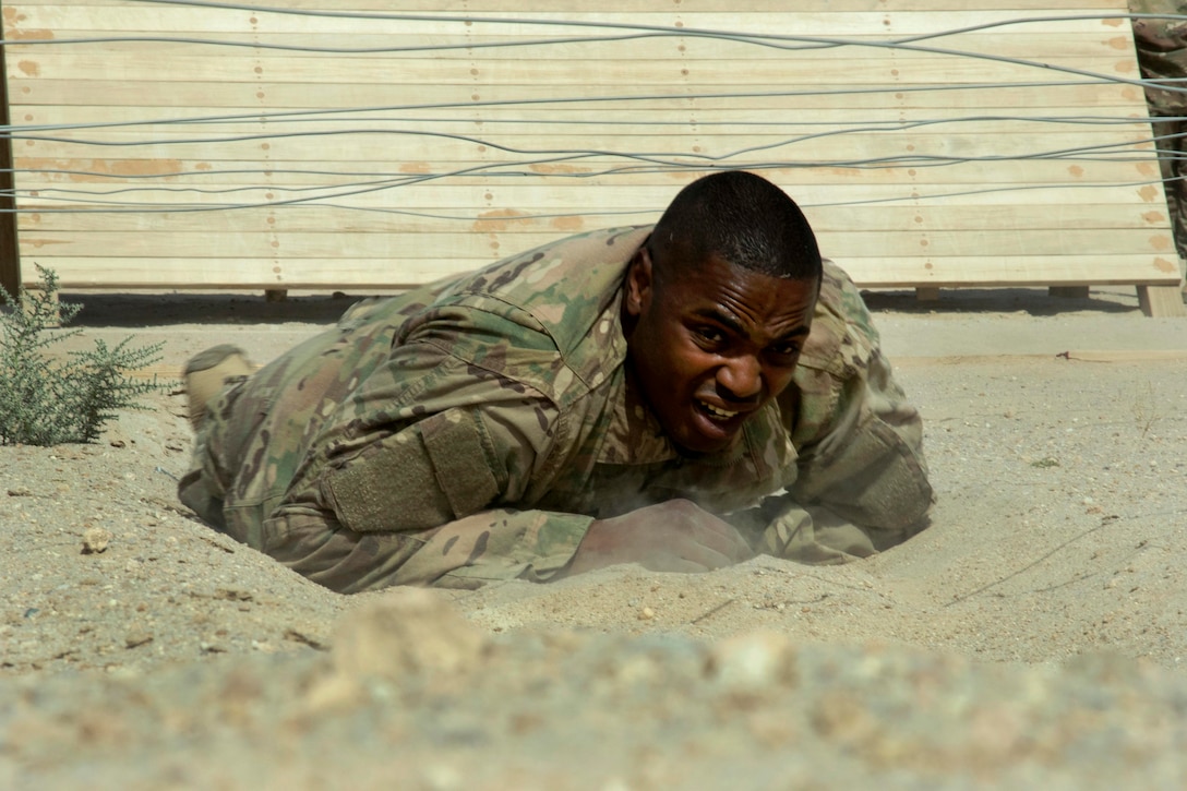 A soldier low crawls under a wire obstacle.