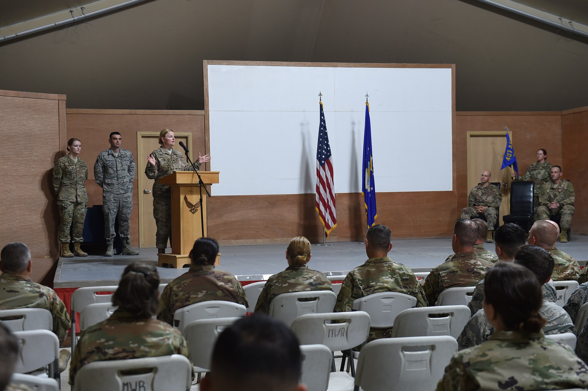 An Airman stands behind a podium and speaks to the audience