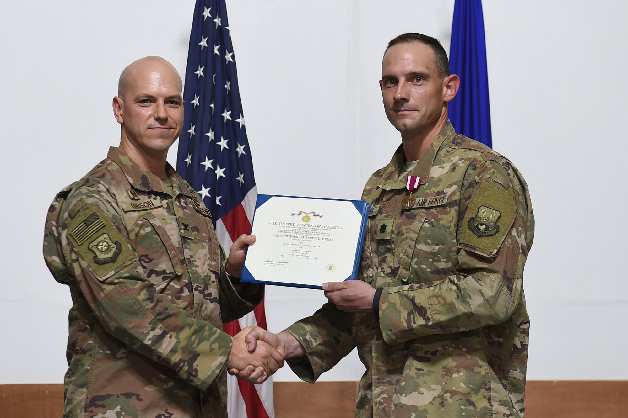 two airman shake hands and pose for a picture