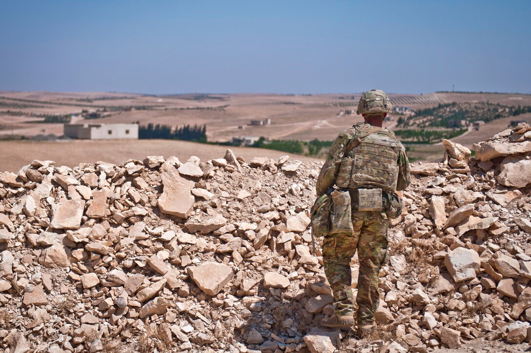 A soldier provides security from behind a rock pile berm.