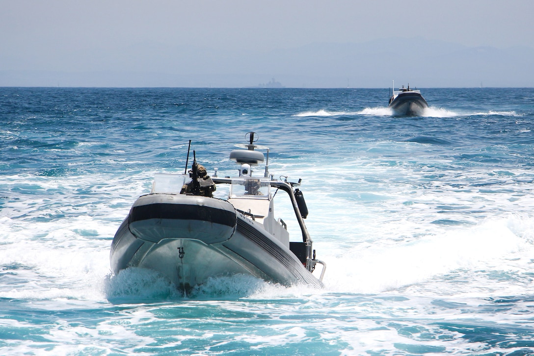 U.S. Coast Guard members and Canadian sailors in high-speed boats approach a vessel.