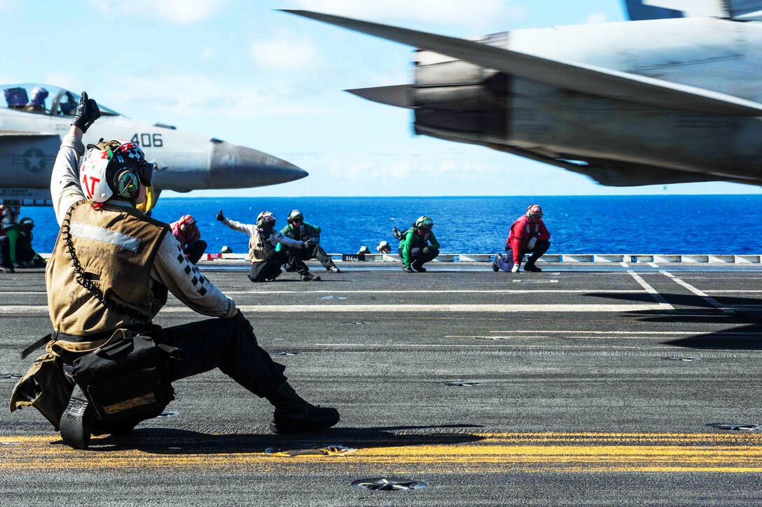 A sailors signals a F/A-18F Super Hornet to launch from the aircraft carrier USS Ronald Reagan.