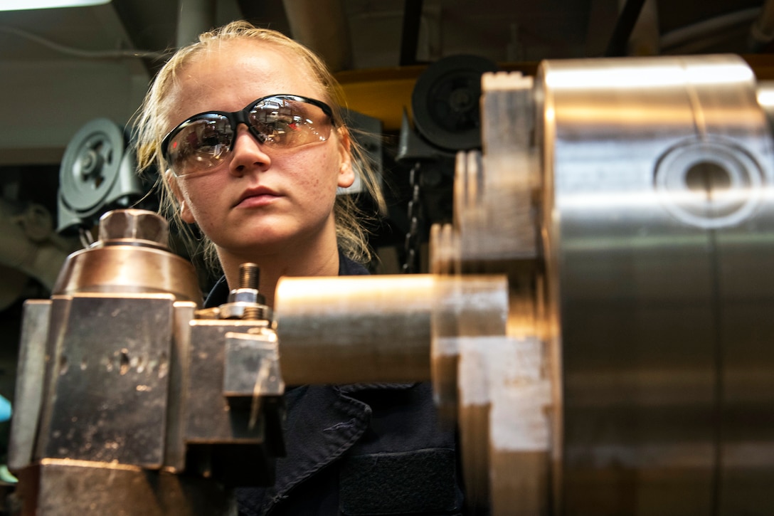 A Navy seaman operates a lathe in the machine shop.