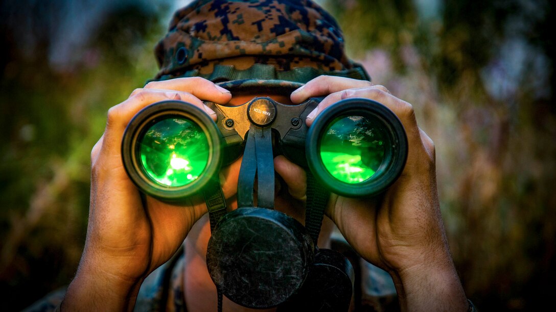 A Marine looks through binoculars with green lenses.