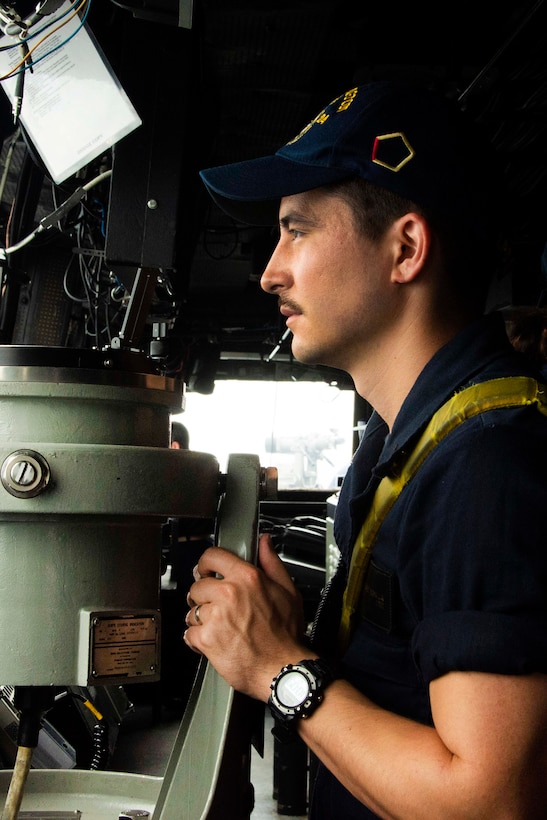 A sailor stands watch in the pilot house of the USS Arlington.