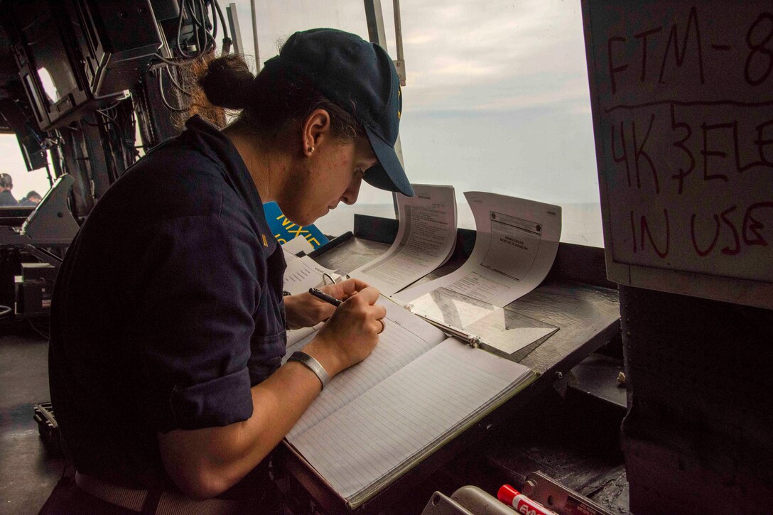 A sailor makes log entries while standing watch in the pilot house of the USS Arlington.