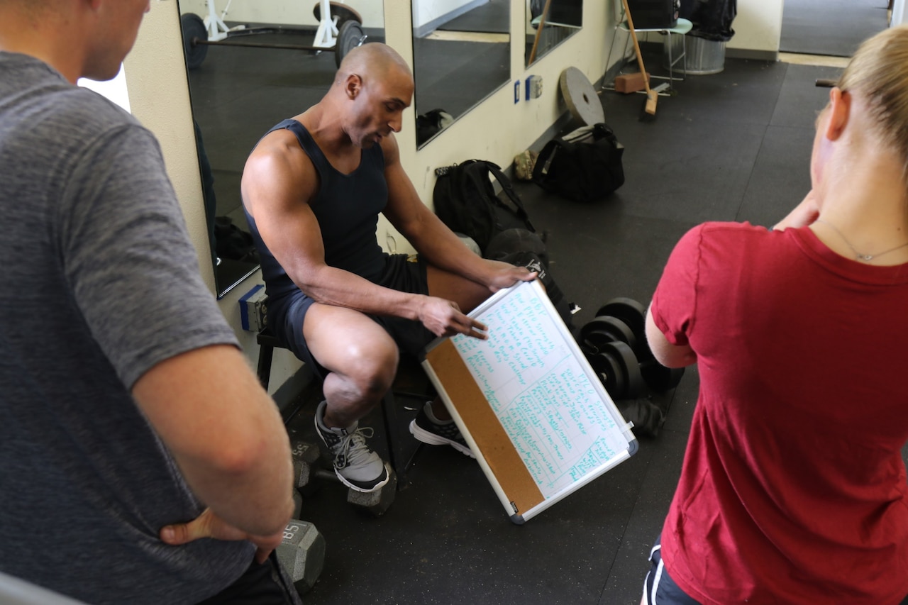 A trainer explains a fitness routine written on a whiteboard.