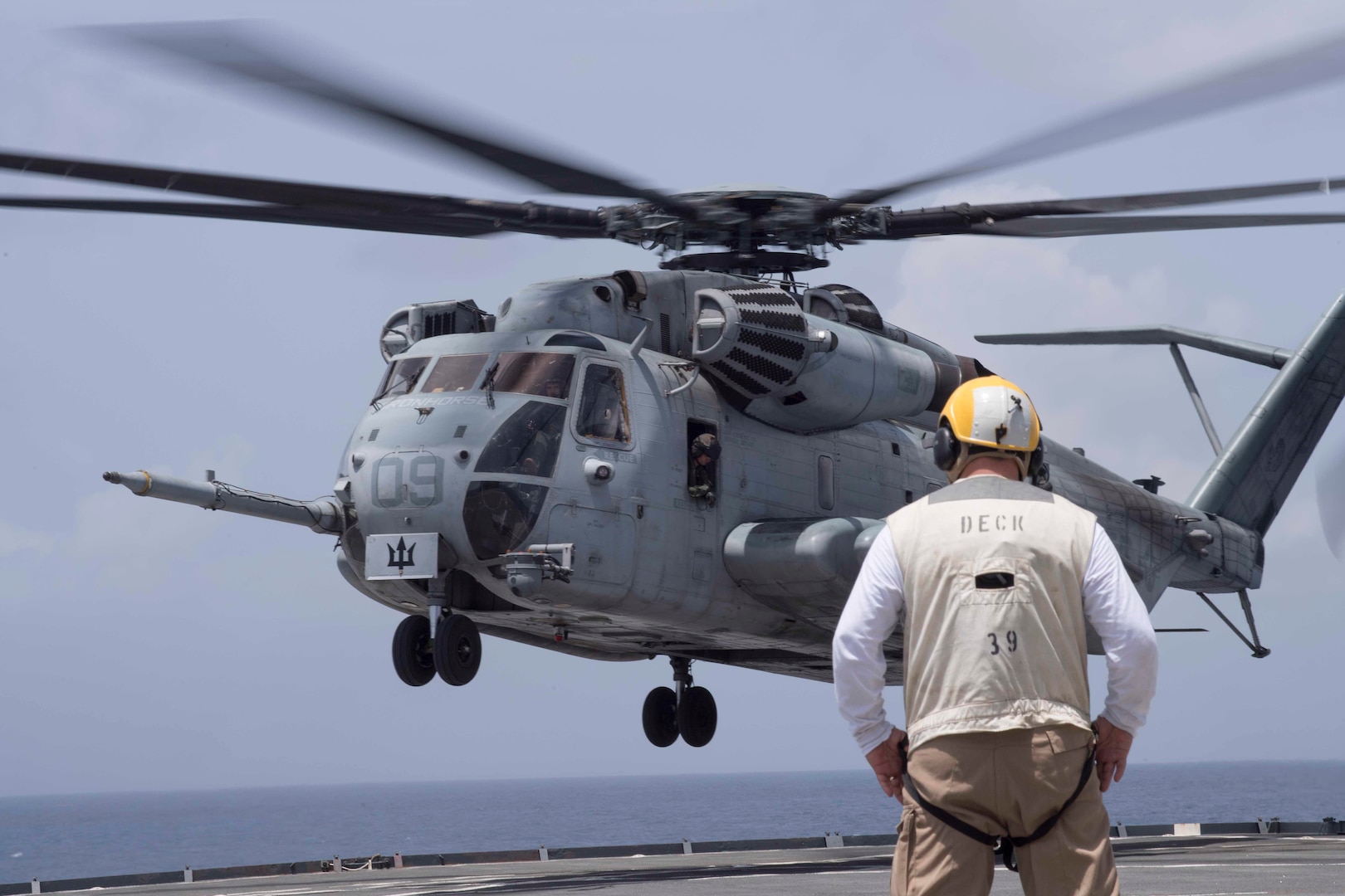 A U.S. Navy sailor watches as a CH-53E Super Stallion helicopter with Special Purpose Marine Air-Ground Task Force - Southern Command comes in for a landing on the flight deck of the USS Gunston Hall while conducting deck landing qualification training off the coast of Belize, July 7, 2018. The Marines of SPMAGTF-SC worked closely with Gunston Hall sailors to qualify six pilots and five enlisted aircrew members responsible for the helicopters’ safe operation. Having qualified Marines provides SPMAGTF-SC with helicopter movement capabilities of personnel and cargo between the shore and ship. The Marines and sailors of SPMAGTF-SC are conducting security cooperation training and engineering projects alongside partner nation military forces in Central and South America. The unit is also on standby to provide humanitarian assistance and disaster relief in the event of a hurricane or other emergency in the region.