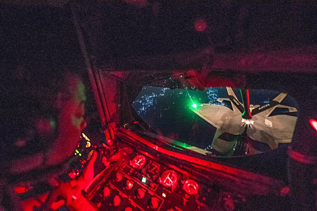 An airman looks out a window toward an aircraft in flight.