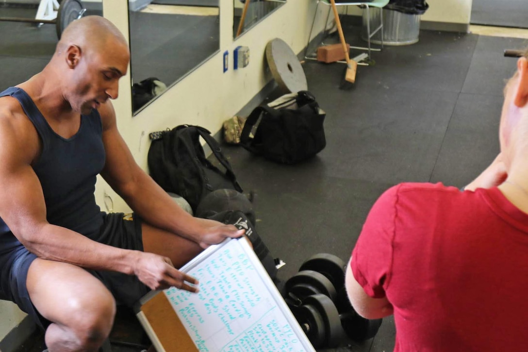 A trainer explains a fitness routine written on a whiteboard.