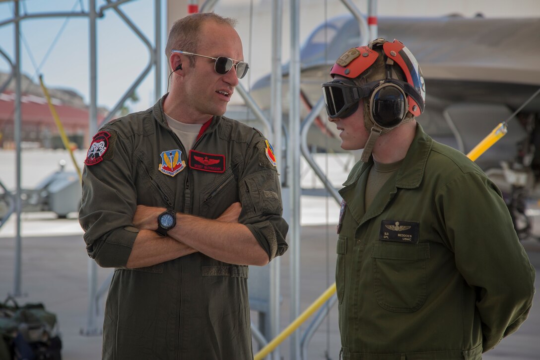 U.S. Airman Maj. Caleb "Skeet" Guthman, a pilot, attached to Hill Air Force Base, Utah, discusses upcoming exercises with U.S. Marine Corps Cpl. Samuel Beddoes, an aviation ordnance technician with Marine Fighter Attack Squadron (VMFA) 122, Marine Corps Air Station (MCAS) Yuma, on MCAS Yuma, Ariz., June 26, 2018. The exercise tested, for the first time, the interoperability of loading weapon systems between the services F-35's. The U.S. Air Force operates with the F-35A Lightning II, while the U.S. Marine Corps operates with the F-35B Lightning II. (U.S. Marine Corps photo by Sgt. Allison Lotz)