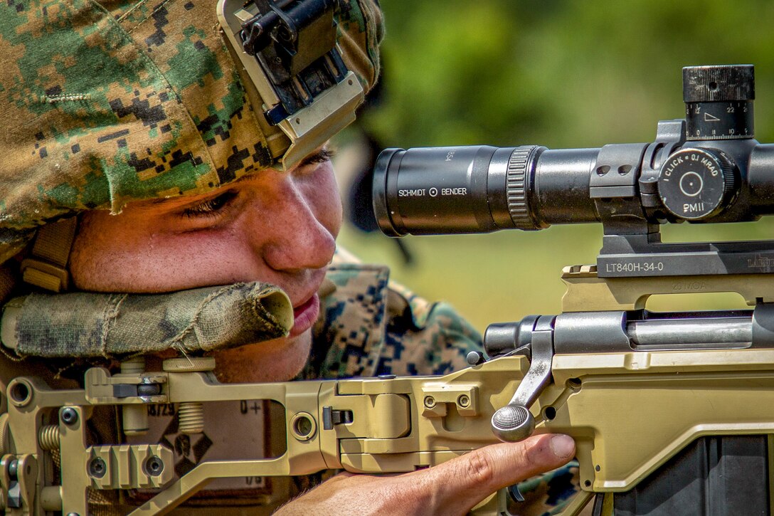 A Marine looks through a scope on a rifle.