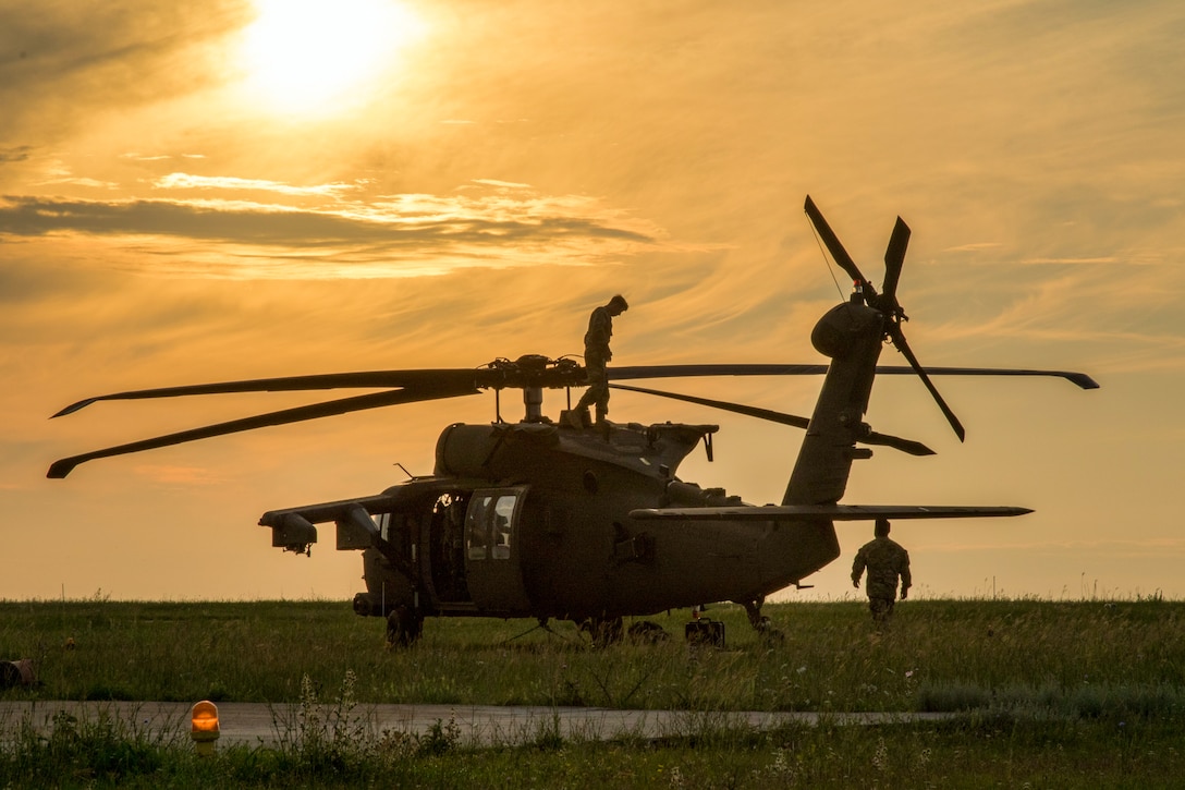 Two soldiers walk around and on top of a helicopter.