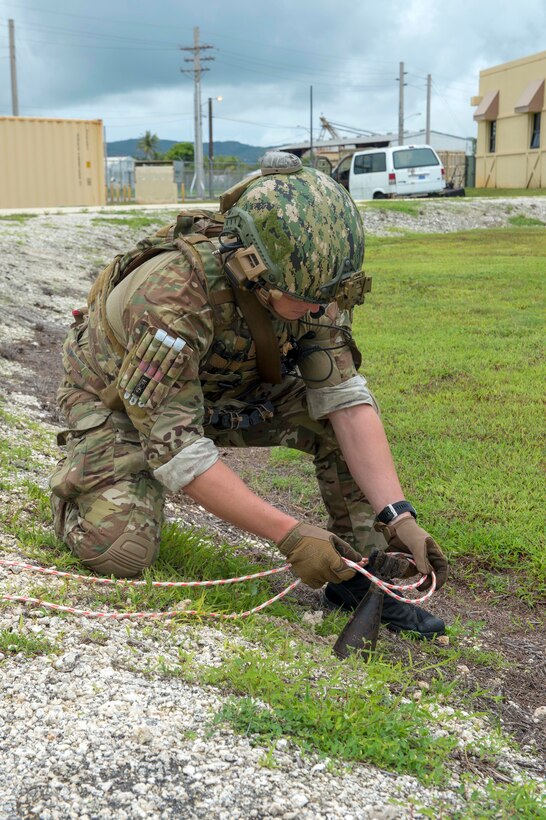 A sailor places a multi-colored rope around a mortar identifying it as unexploded munitions.