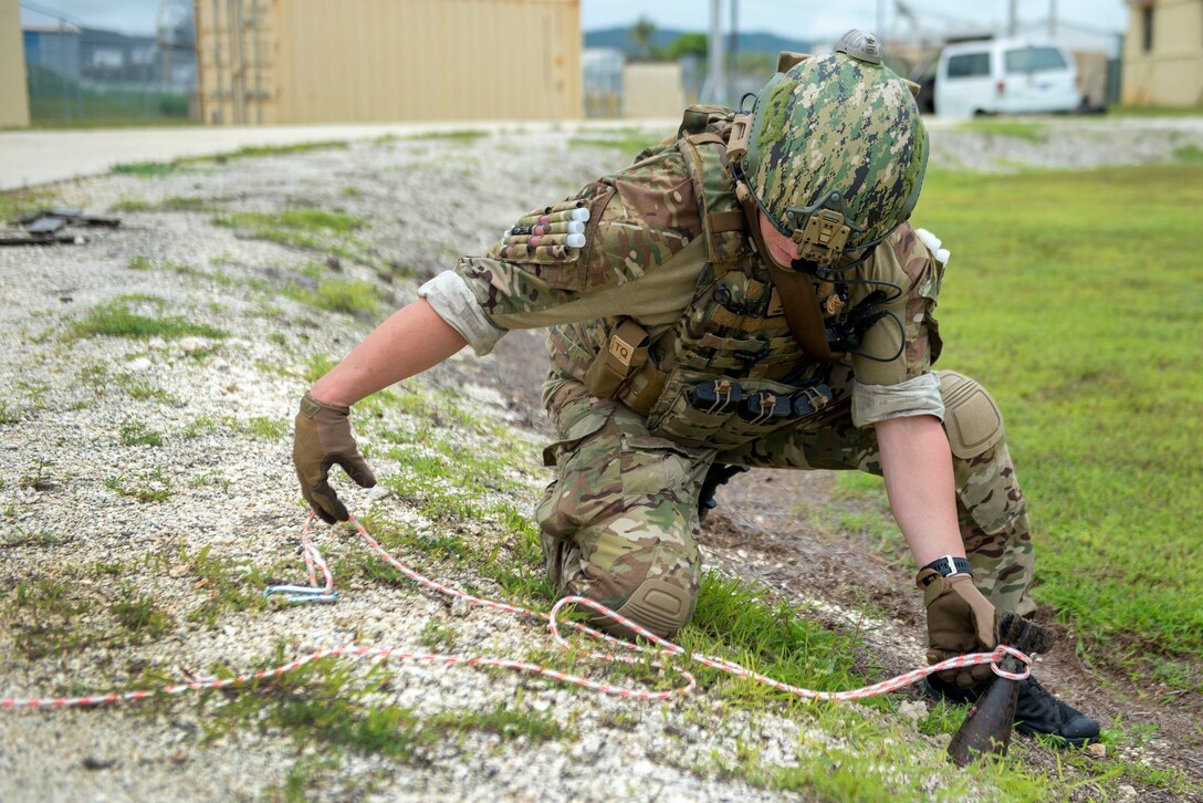 A sailor secures and extends a multi-colored rope around a mortar identifying it as unexploded munitions.