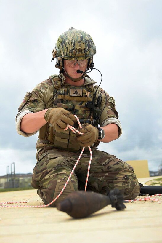 A sailor prepares a multi-colored rope before placing it around a mortar identifying it as unexploded munitions.