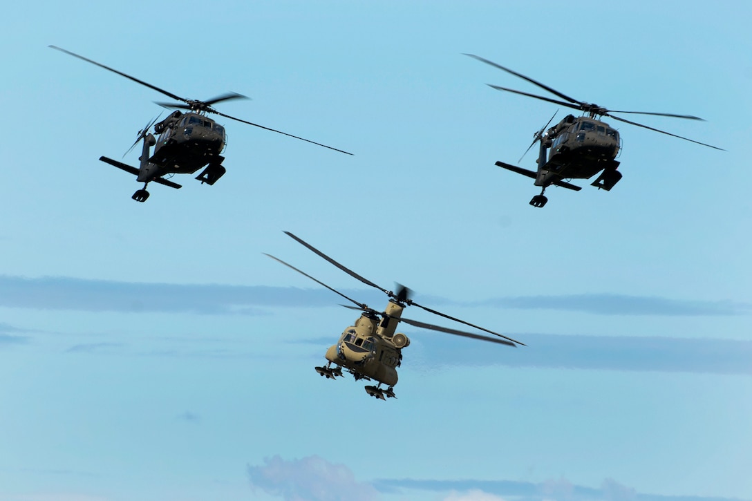 UH-60 Black Hawk helicopters and a CH-47 Chinook helicopter fly in formation while approaching the flight line.