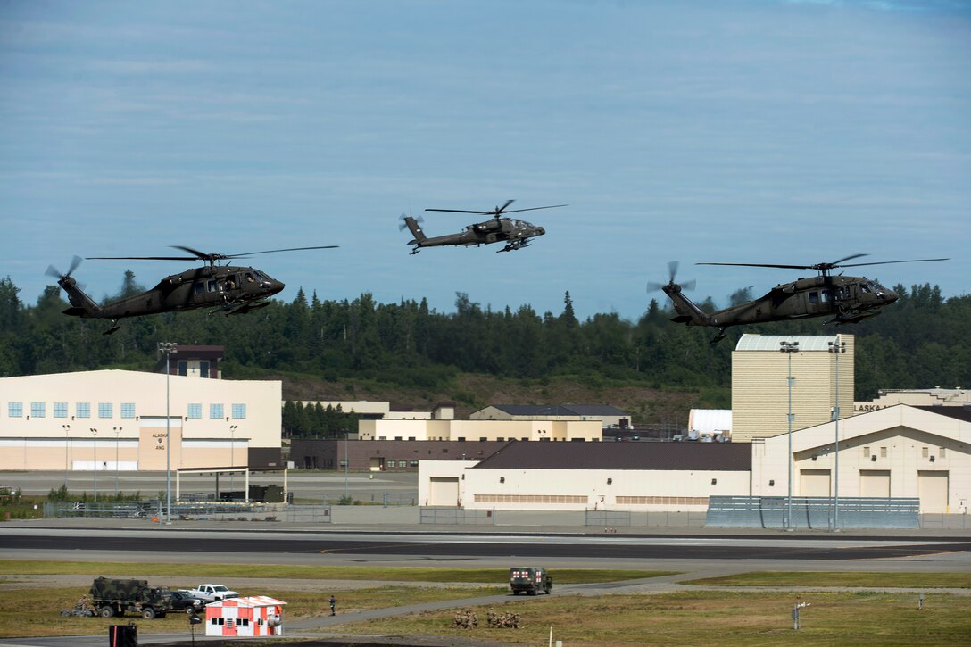 Two UH-60 Black Hawk helicopters and an AH-64 Apache helicopter prepare to land.