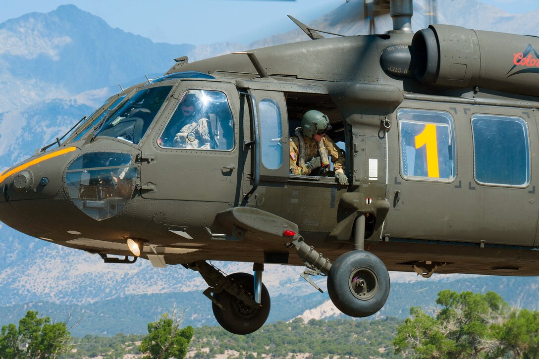 A helicopter pilot takes off while a crew chief checks for proper clearance.