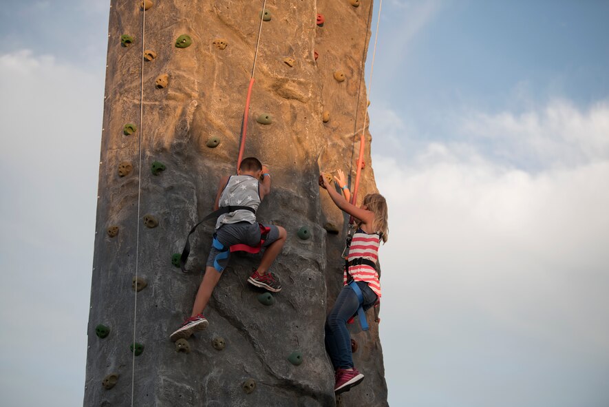 Two children climb up a rock wall prior to an Intel drone light show at Travis Air Force Base, Calif., July 5, 2018. The event featured numerous activities including music, bounce houses and an eight minute light show with 500 drones. (U.S. Air Force photo by Tech. Sgt. James Hodgman)