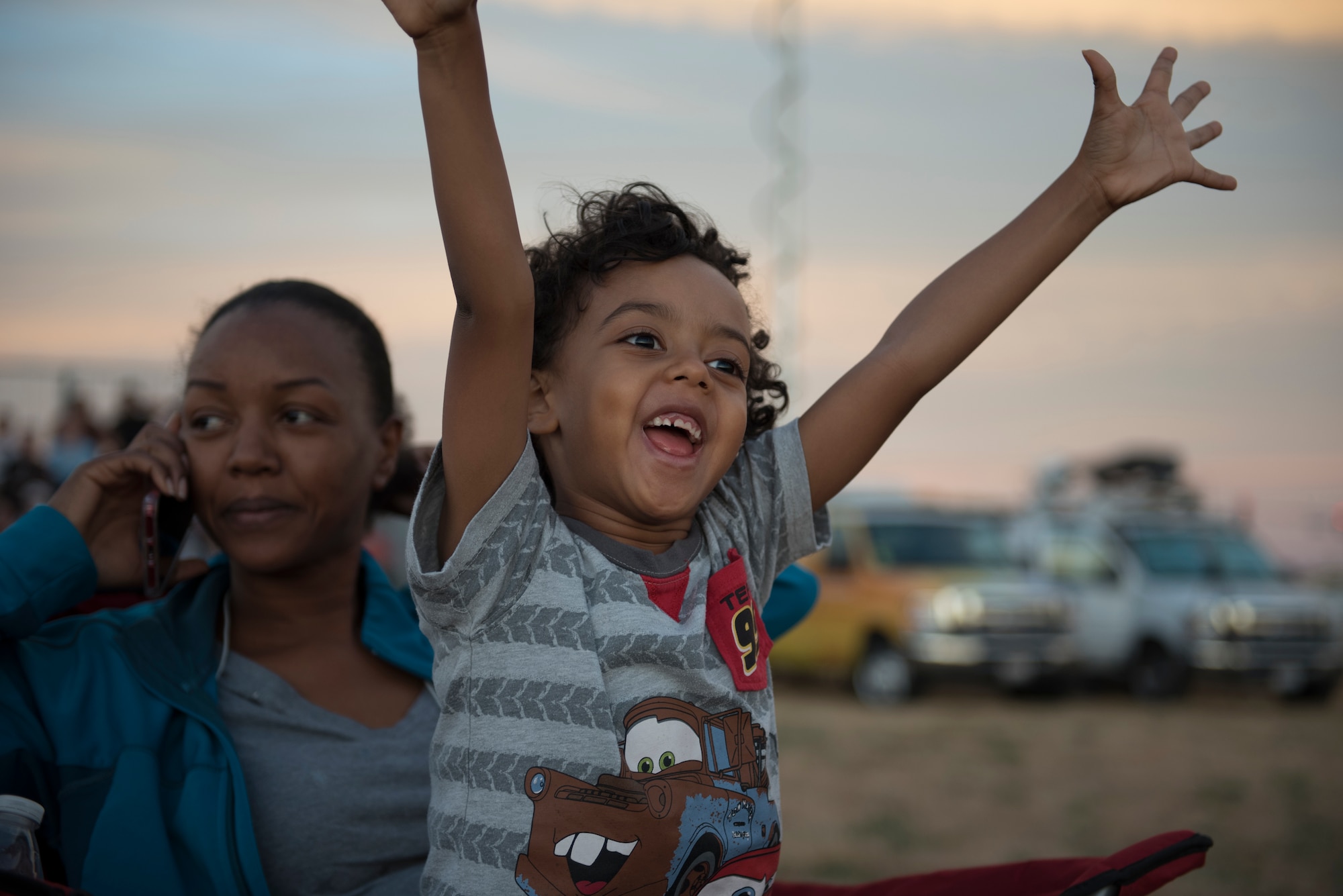 Mekhi Hodgman, 5, shows his excitement as he waits for the start of the Intel Shooting Star Drone light show, while his mother, Joyce Hodgman, a community based therapist, answers a phone call at Travis Air Force Base, Calif., July 5, 2018. The event featured numerous activities including music, bounce houses and an eight minute light show with 500 drones. (U.S. Air Force photo by Tech. Sgt. James Hodgman)