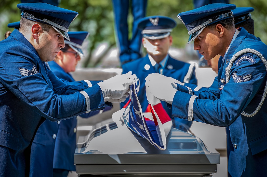 Airmen fold an American flag over a casket.