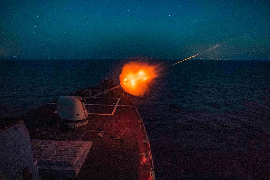 A ship fires a gun at night.